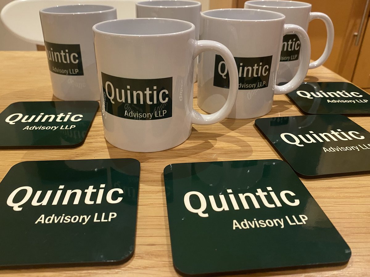 Mugs and coasters printed with a client's company logo, arranged on a wooden table